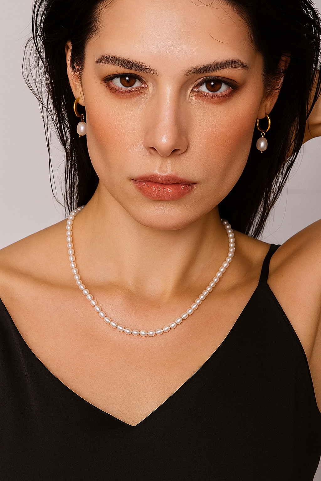 Woman wearing a pearl necklace and earrings against a neutral background